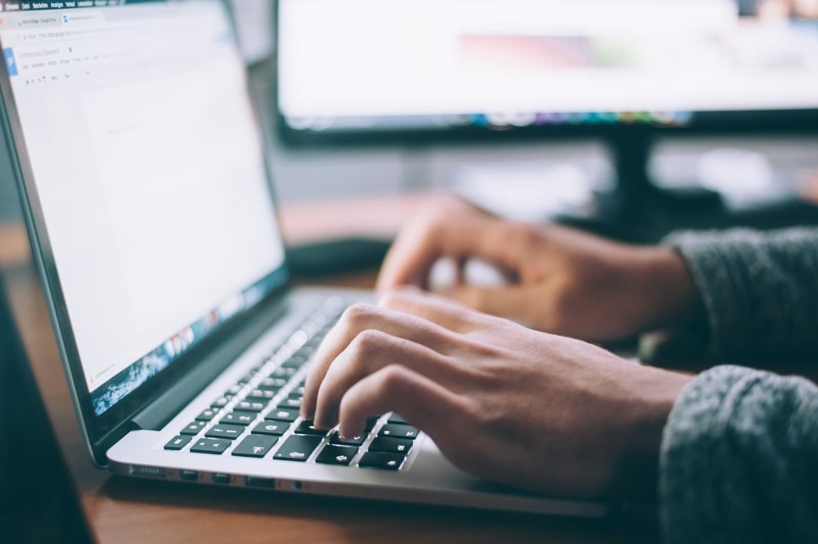 Hands typing on a laptop with a second monitor in the background — representing endpoint device protection