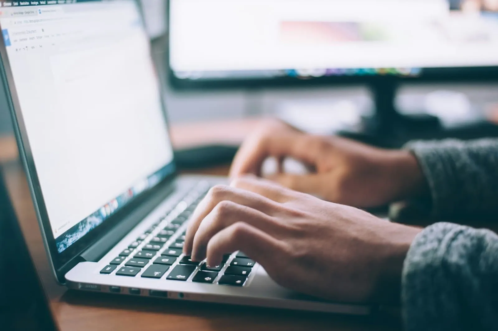 Hands typing on a laptop with a second monitor in the background — representing endpoint device protection